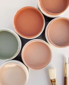 four paint cans with different colors and brushes next to one that has been painted on