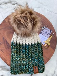 a knitted hat with a fur pom sits on top of a wooden table