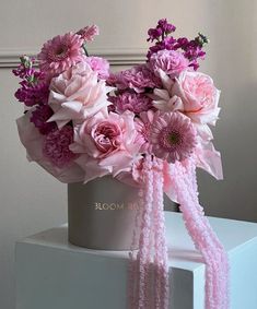 a bouquet of pink flowers in a gray vase on top of a white cubed box