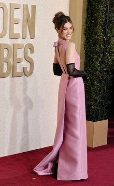 a woman in a pink gown and black gloves on the red carpet at an event