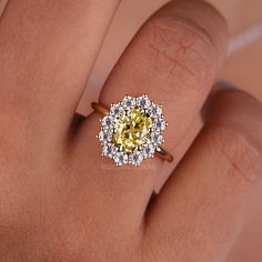 a fancy yellow diamond ring on someone's finger with the center stone surrounded by small white diamonds