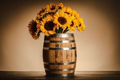 sunflowers are in a wooden barrel on a table with a brown wall behind them