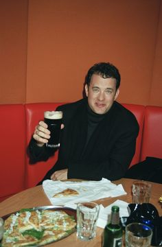 a man sitting at a table with pizza and beer