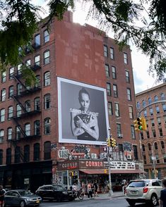 a large advertisement on the side of a tall building in a city with cars and pedestrians