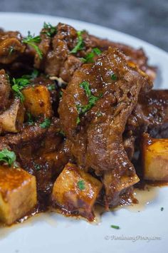 a white plate topped with meat covered in gravy and garnished with parsley