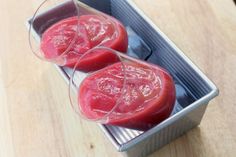 two glasses filled with red liquid sitting on top of a wooden table next to a metal container