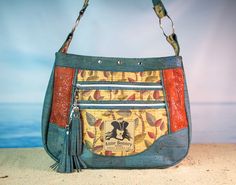 the purse is on the sand by the water and it has a tasseled handle