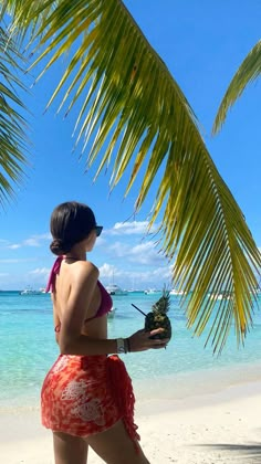 a woman in a red and white bathing suit holding a pineapple on the beach