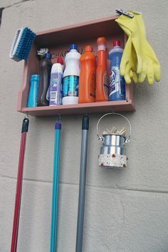 an assortment of cleaning products and tools hanging from a shelf on the wall next to a broom