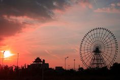 the sun is setting behind a ferris wheel