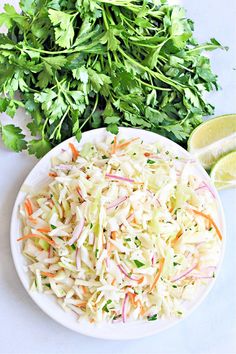 a white plate topped with coleslaw next to sliced limes and cilantro