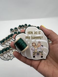 a hand holding a green spool of thread and a button with the words how big is my tummy?