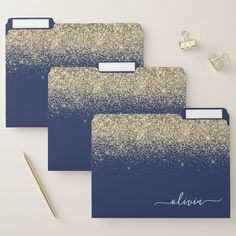 three blue and gold glittered file folders with name on them, next to a pen