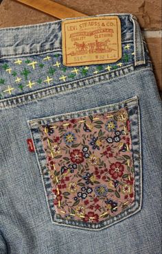 the back pocket of a pair of jeans with crosses and flowers on it, sitting on a wooden floor