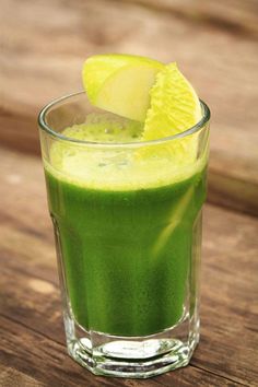 a glass filled with green liquid and a slice of lemon on top of the drink