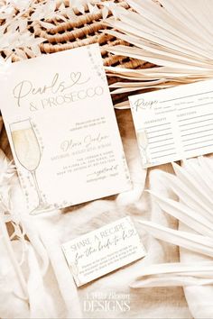 the wedding stationery is laid out with wine glasses and fanned palm fronds