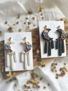 three pairs of earrings with flowers on them sitting in front of a card and some confetti