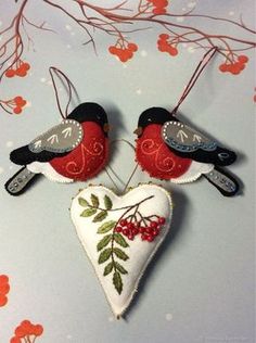 two red and black birds sitting on top of a heart shaped ornament with berries