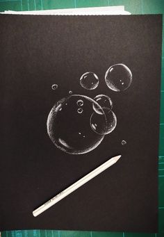 a drawing of soap bubbles on black paper with a white pencil next to it and green background