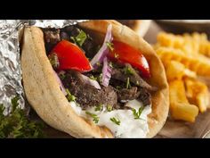 a pita filled with meat and vegetables on top of a wooden cutting board next to fries