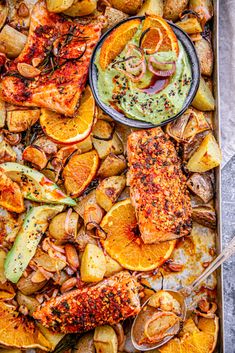 a pan filled with salmon and potatoes covered in green sauce, garnished with herbs