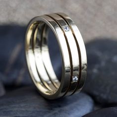 two gold wedding bands with white diamonds on them, sitting on some rocks in the sun