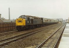 a yellow and black train traveling down tracks next to a bricked building on a foggy day