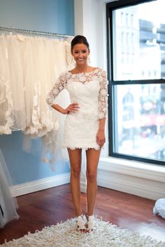 a woman standing in front of a window next to a wedding dress on a hanger