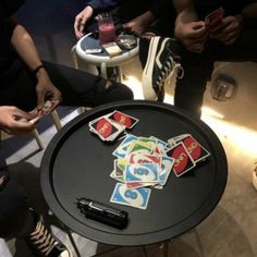 several people sitting around a table with playing cards on it and one person holding a cell phone