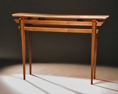 a wooden table sitting on top of a white floor next to a black wall with light coming through it