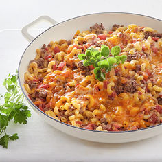 a white dish filled with macaroni and cheese on top of a table next to parsley