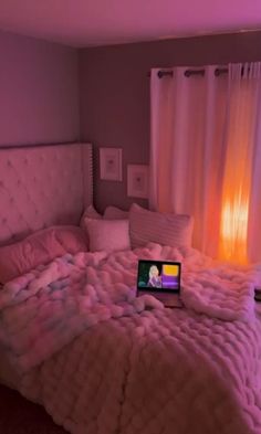 a laptop computer sitting on top of a bed in a room with pink walls and curtains