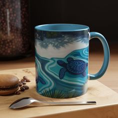 a coffee mug sitting on top of a wooden table next to a spoon and cookie