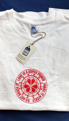 a white t - shirt with a red clover on the front and a tag attached to it