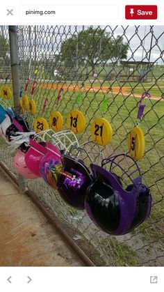 a fence with many different colored helmets hanging on it's sides and numbers painted on them