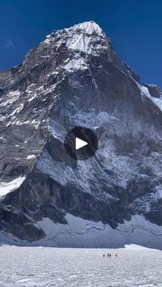 a large mountain with snow on it and people walking in the snow near by,