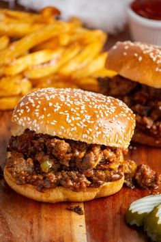 two sloppy joes are sitting on a wooden table next to french fries and ketchup