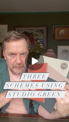 a man sitting at a table holding up some type of sign that says three schemes using studio green