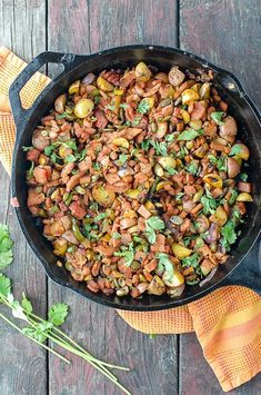 a skillet filled with beans and greens on top of a wooden table next to an orange towel