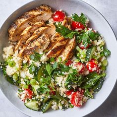 a white bowl filled with chicken, rice and veggies on top of a table