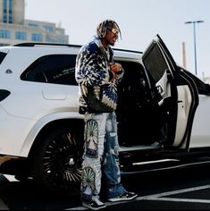 a man standing in front of a white suv with the door open and looking at his cell phone