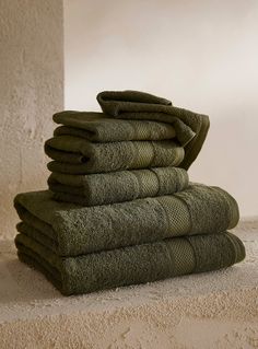 a stack of folded green towels sitting on top of a stone floor next to a wall