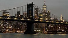 the city skyline is lit up at night as seen from across the water in front of the brooklyn bridge