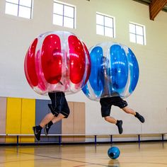 two people are jumping through inflatable balls on a gym floor with one person running behind them