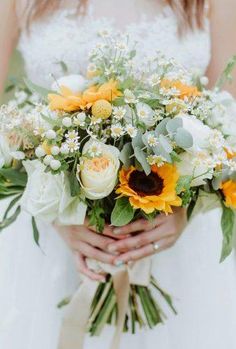 a bride holding a bouquet of sunflowers and other flowers on her wedding day