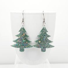 Fun Christmas tree dangle earrings featuring Frosty Green glitter with Rainbow shards mixed with crystal clear epoxy resin, and finished with Stainless Steel ear wires with soft silicone backs.  Clear epoxy coated for a glossy protective layer.  Festive holiday earrings measure 2 1/2 inches long and 1 1/2 inches wide and are very lightweight.  These earrings make the perfect Christmas party accessory, stocking stuffer and Secret Santa gift.   ⭐ CARE   Wipe clean with a soft cloth (such as an eyeglass cleaning cloth).  Do not use alcohol or acetone as this will damage the glossy surface.  It is not recommended to wear in water.  Do not expose to extreme heat.  To extend the life of your resin pieces, store separately from other jewelry and keep out of direct sunlight whenever possible. Christmas Party Jewelry With Sparkling Details, Sparkling Christmas Party Jewelry, Sparkling Jewelry For Christmas Party, Christmas Party Accessories, Crystal Clear Epoxy Resin, Clear Epoxy Resin, Holiday Earrings, Cool Christmas Trees, Clear Epoxy