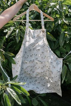 an apron hanging on a tree branch with leaves in the foreground and someone's hand reaching for it