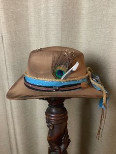 "This is a custom weathered hat with incredible detail.  Tan felt hat with blue western fabric.  Black and brown hat band with silver studs, silver bull and raw hide ties.  Stitching on top and burnt playing card.  Jute rope tied around.  Authentic peacock and blue jay feather.  Wood burned Ivy and verse \"Delight In The Lord\".  Adjustable band inside to fit any size." Luxury Artisan Felt Hat For Western-themed Events, Distressed Brown Brimmed Hat For Western-themed Events, Bohemian Felt Hat With Feathers For Western-themed Events, Feathered Felt Hat With Flat Brim For Western-themed Events, Western-themed Fedora With Feathers, Blue Jay Feather, Jay Feather, Velvet Gloves, Painted Hats