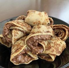 chocolate covered crepes stacked on top of each other in a black plate with a wooden table