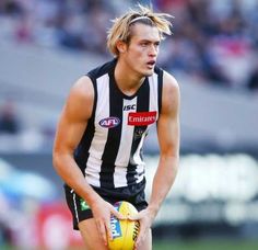 a male afl player holding a ball in his hand and looking to the side with one foot